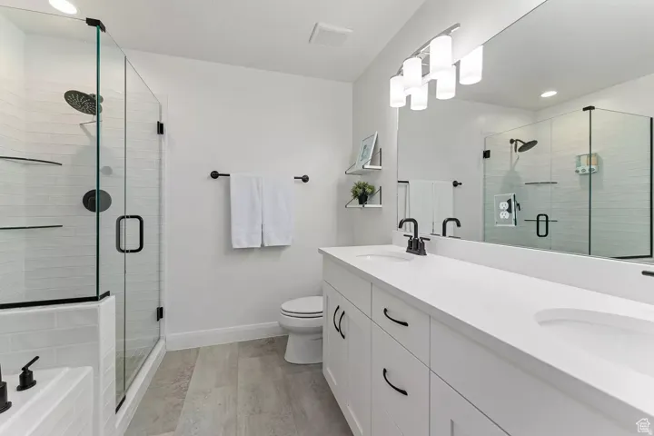 Bathroom with double vanity, recessed lighting, a stall shower, a tub to relax in, and light wood-style floors