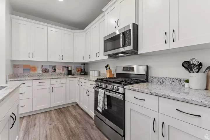 Kitchen with stainless steel appliances, white cabinetry, light stone countertops, and light wood-type flooring