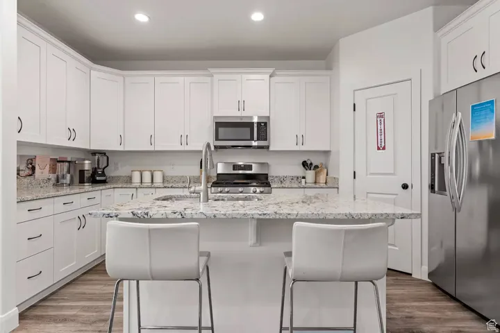 Kitchen featuring stainless steel appliances, white cabinetry, light stone counters, a kitchen island with sink, and recessed lighting
