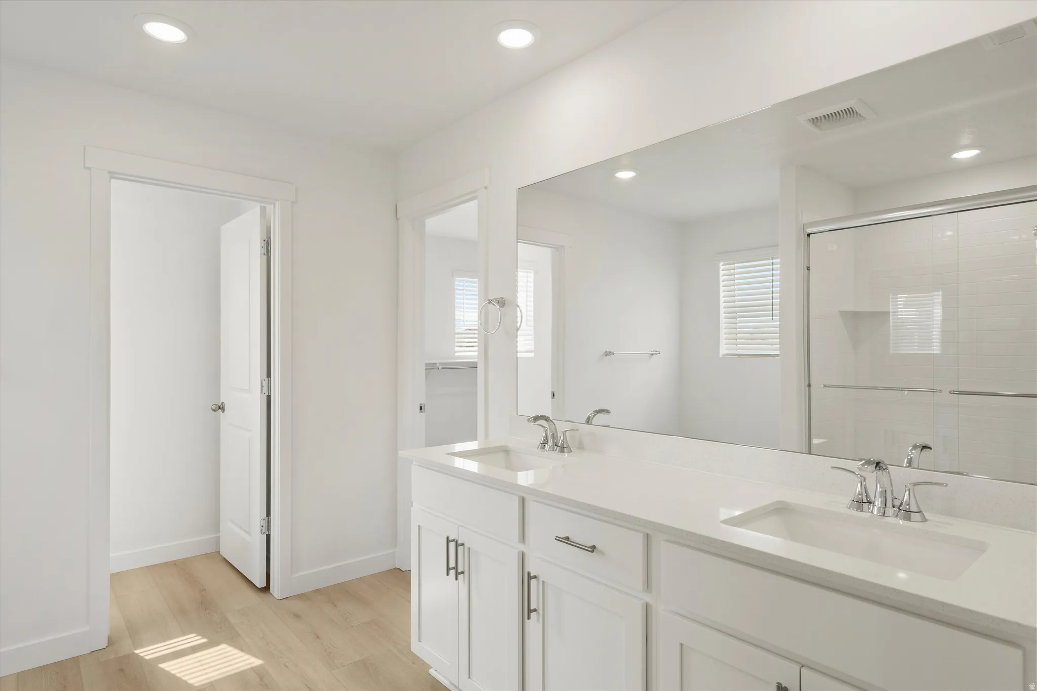 **DISCLAIMER** Interior colors & finishes may vary.Bathroom with double vanity, light wood finished floors, a stall shower, and recessed lighting