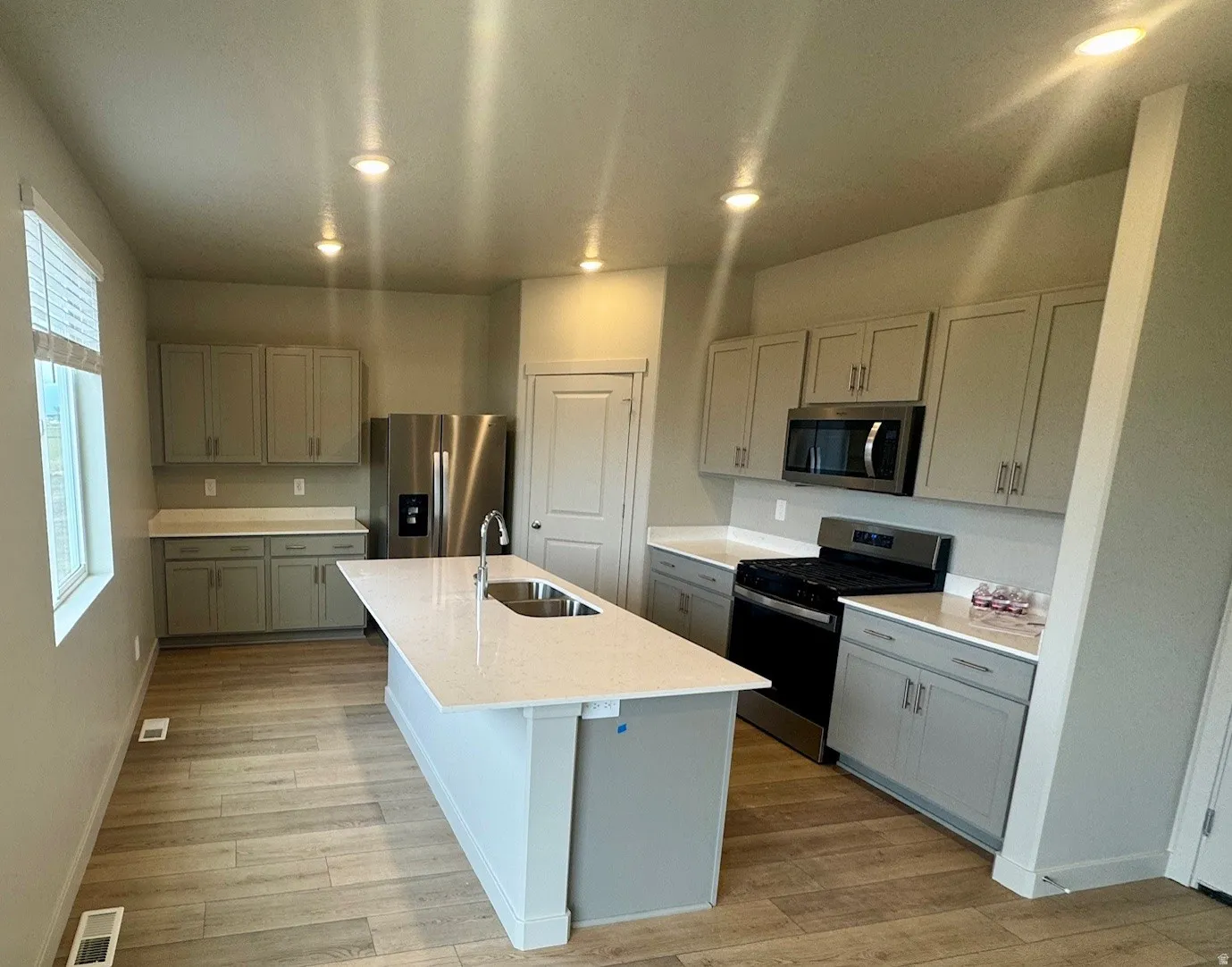 Kitchen featuring appliances with stainless steel finishes, recessed lighting, light stone countertops, an island with sink, and gray cabinets