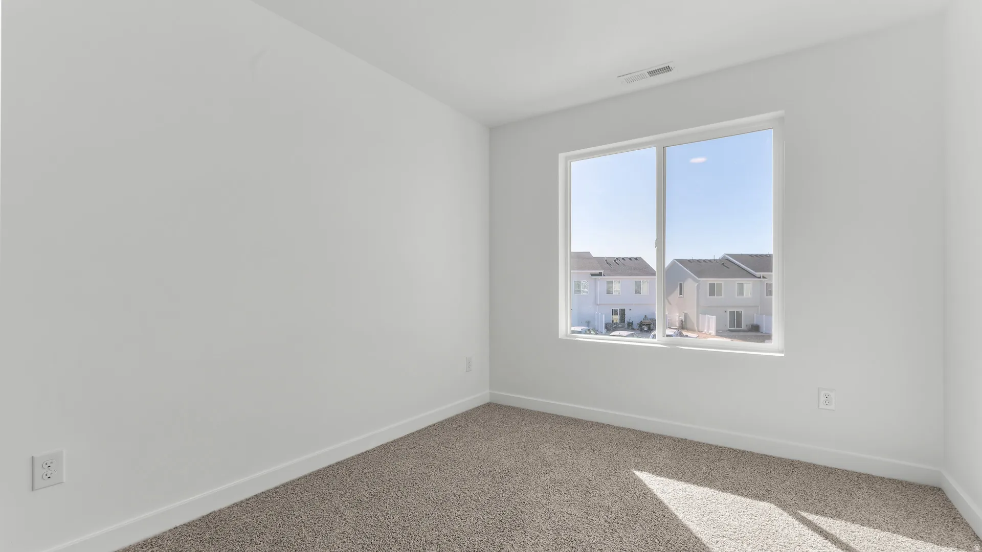 Bright room featuring a large window, neutral carpeting, white walls, and clean baseboards