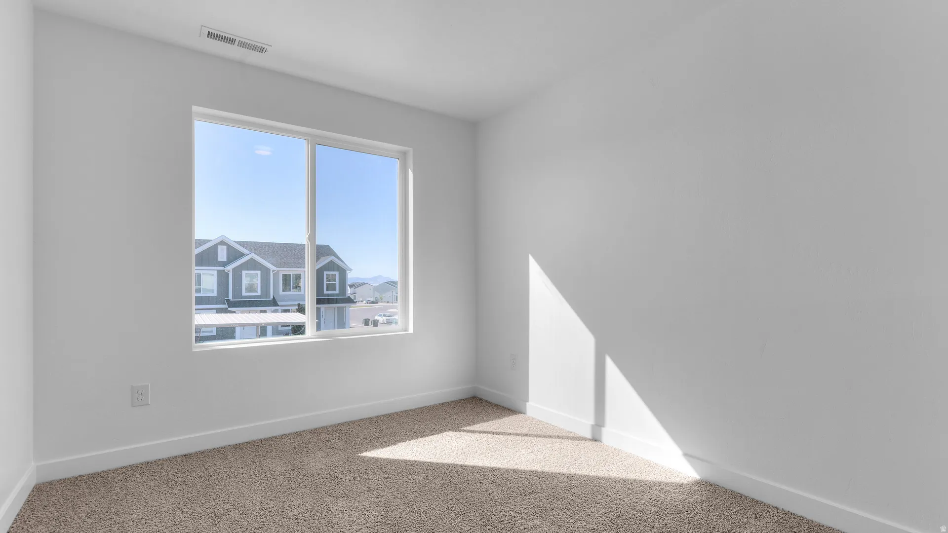Interior room featuring a large double-pane window, neutral-toned carpet, white painted walls, and white baseboards
