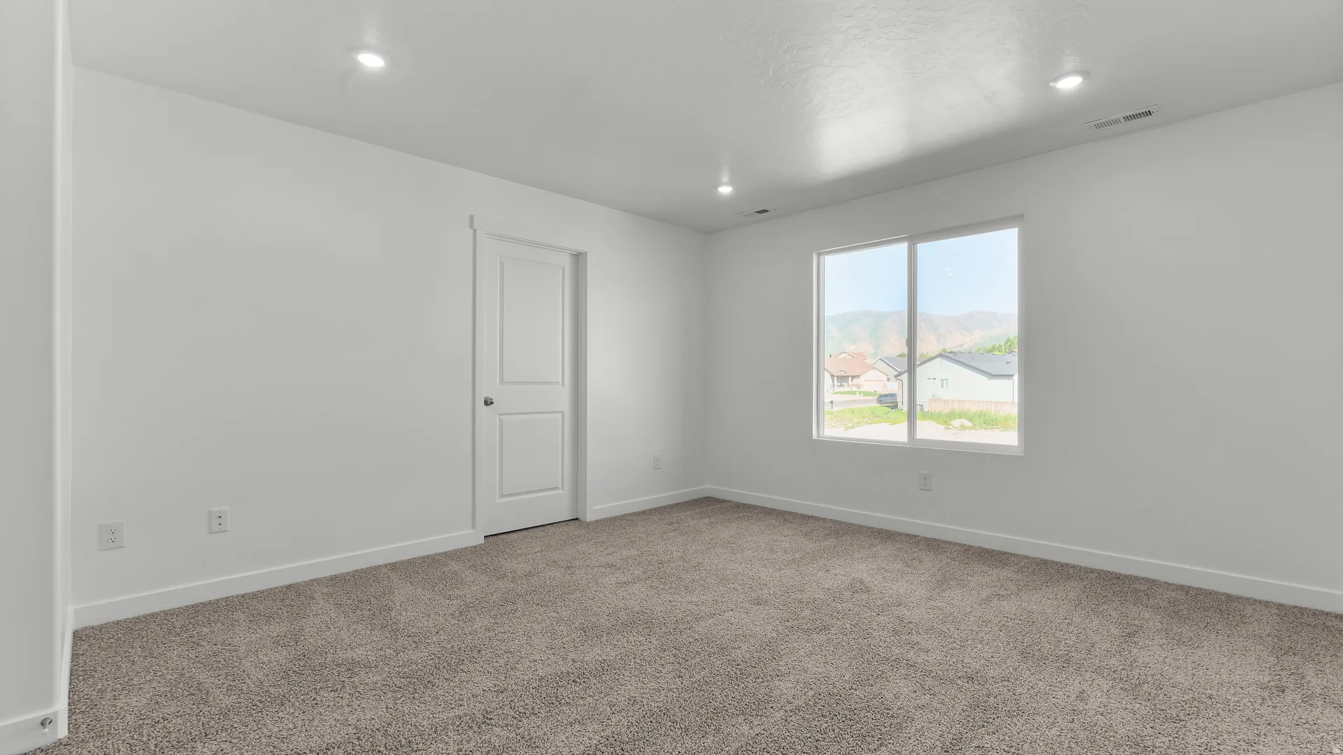 Spacious room featuring neutral carpeting, recessed lighting, white trim, a single window, and a white interior door