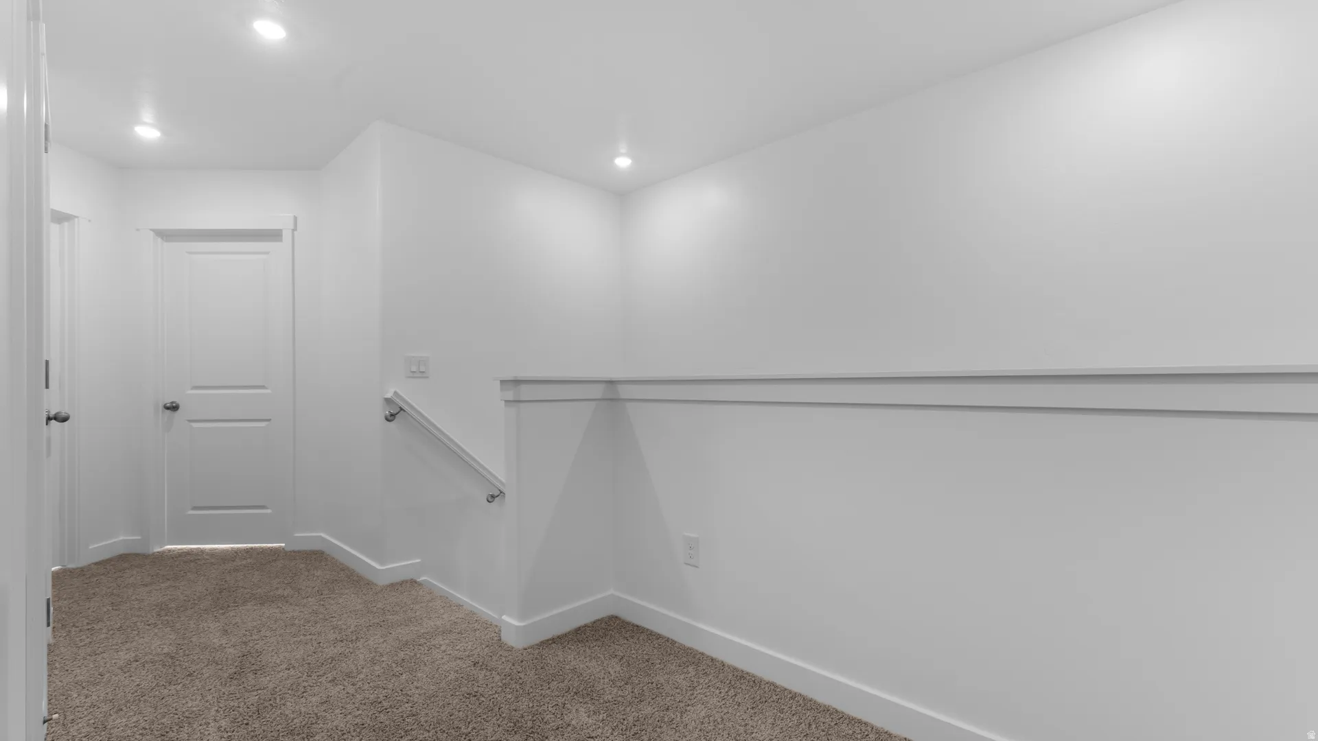 Crisp white walls with chair rail molding, recessed lighting, neutral carpeting, and a white interior door with panel detailing