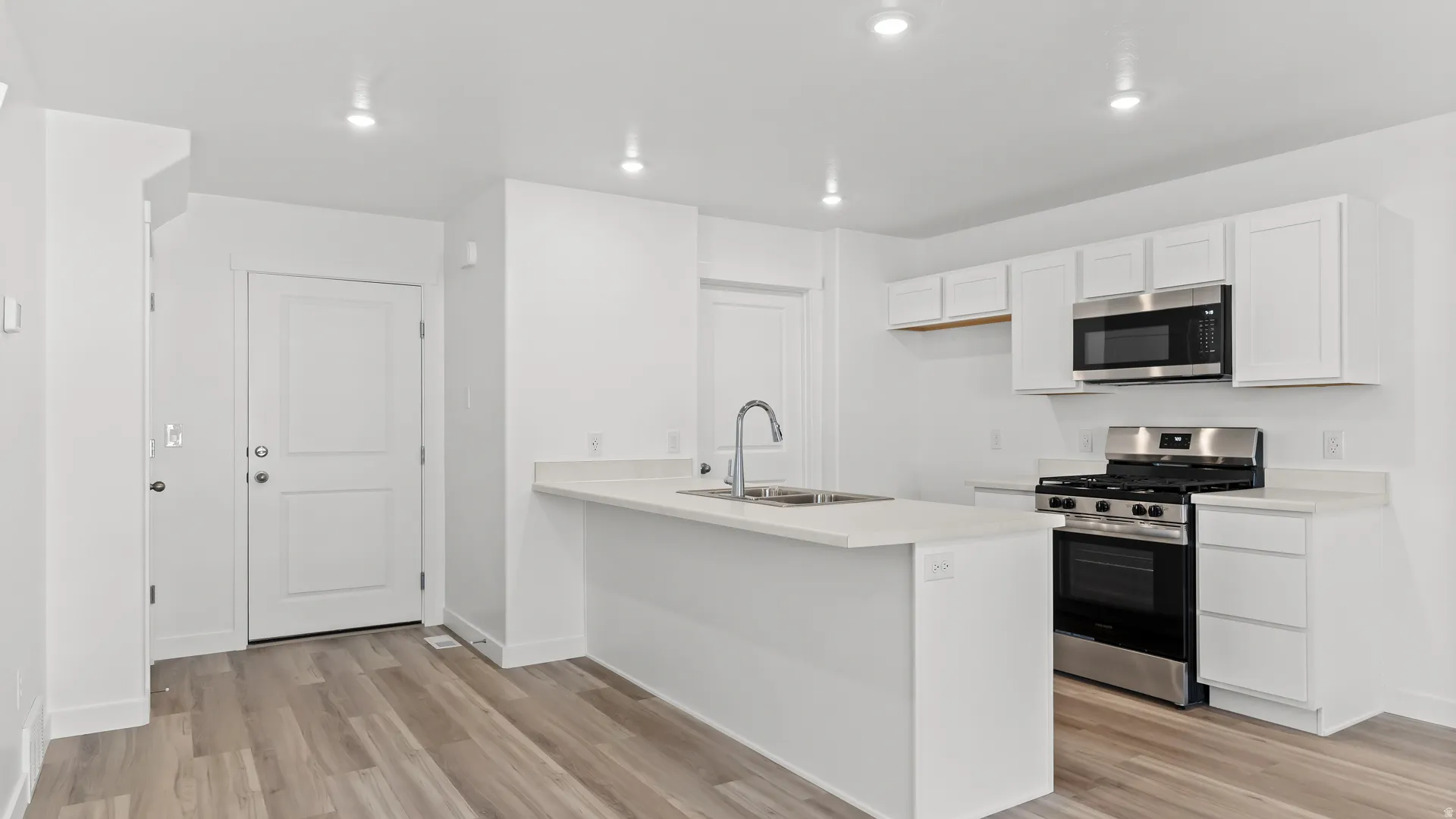 Modern kitchen featuring white cabinetry, light-toned countertops, stainless steel appliances, and a central island with an integrated sink