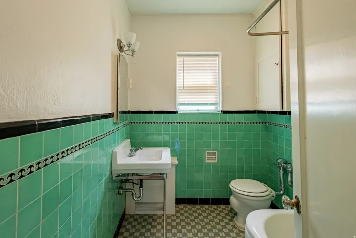 Bathroom featuring vibrant green tile walls with black trim and a decorative border