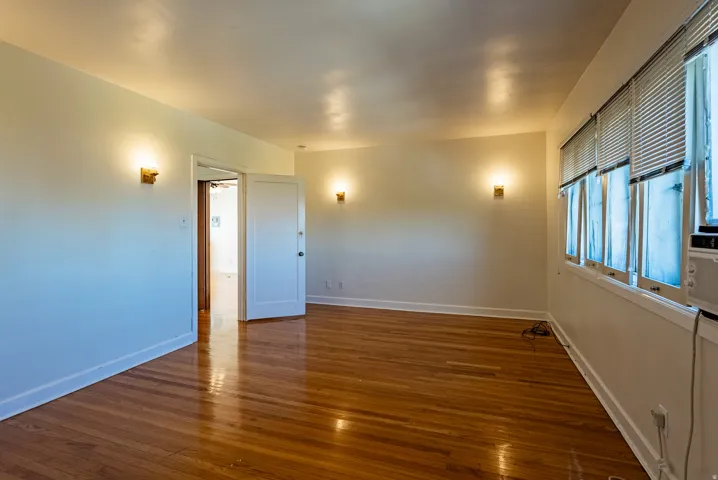 Hardwood flooring in a room with white walls, multiple windows, and wall sconces