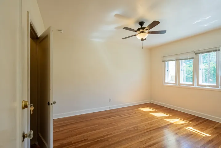 Room featuring wood-finish flooring, a ceiling fan with integrated lighting, and multiple windows