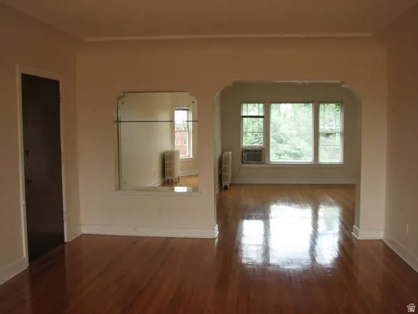 Apt # 8 > Empty room featuring wood finished floors, radiator heating unit, and arched walkways
