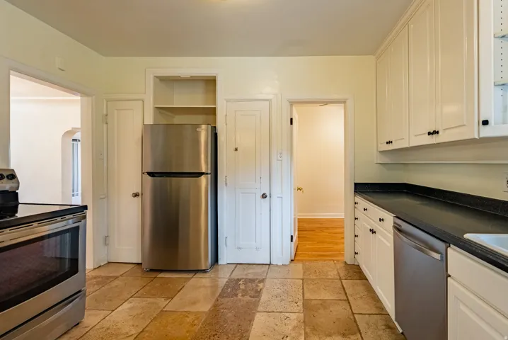 Kitchen featuring stone tile flooring, white cabinetry with black hardware, stainless steel appliances, and dark countertops