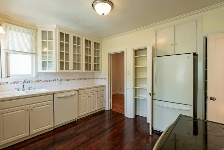 Kitchen featuring rich wood-finish flooring, white cabinetry with glass-front upper units, white tile countertops, and a full-size white refrigerator