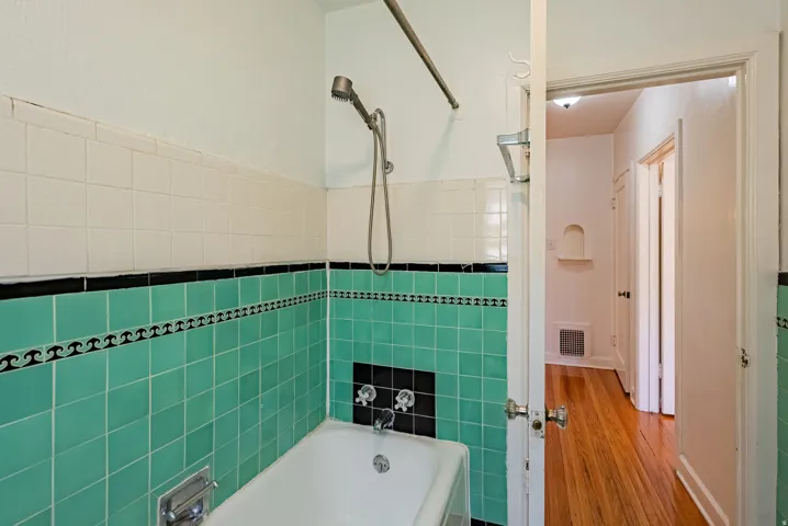 Bathtub and shower combination featuring teal and white tiled walls with decorative trim