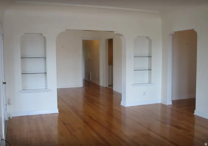 Apt # 5 > Unfurnished room with built in shelves, arched walkways, and light wood-style flooring