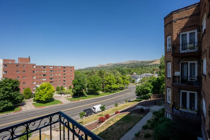 Balcony with wrought iron railing, offering views of a paved road and established trees