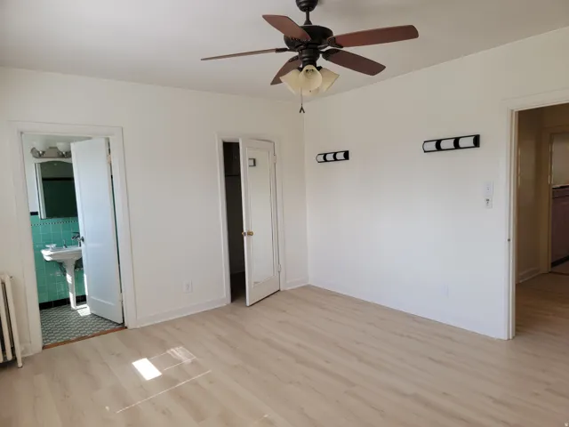 Apt # 10 > Unfurnished bedroom with light wood-style flooring, a ceiling fan, a spacious closet, and radiator heating unit