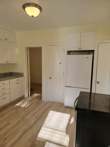 Apt # 9 >  Kitchen with white cabinetry, black electric range, freestanding refrigerator, light wood-style floors, and dark stone counters