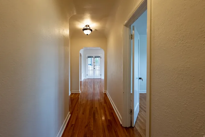 Hallway featuring hardwood flooring, an arched entryway, and a decorative flush-mount light fixture