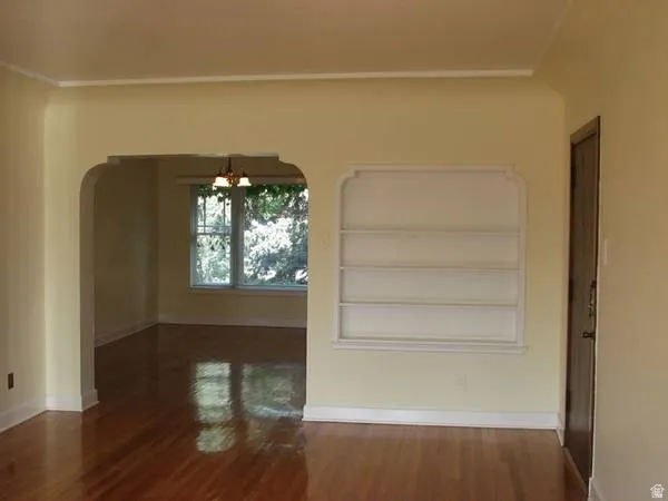 Apt # 11 > Unfurnished room featuring dark wood-style flooring, arched walkways, built in features, a chandelier, and crown molding