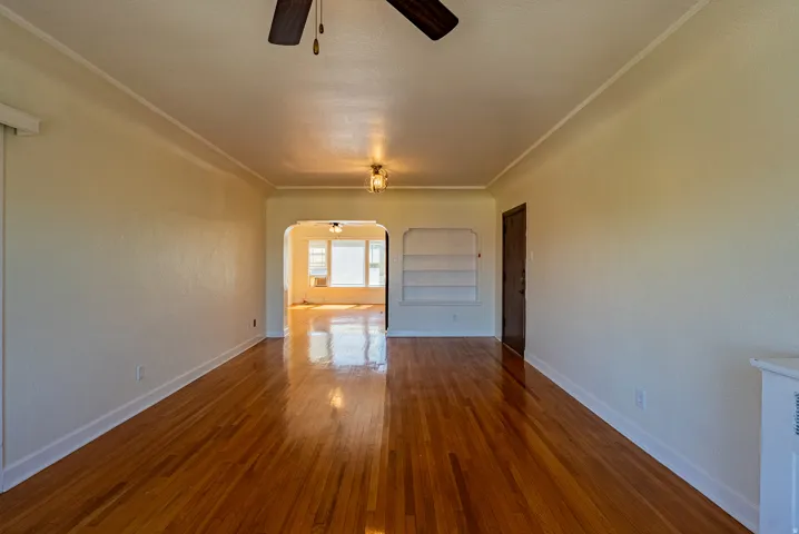 Spacious living area featuring warm wood-finish flooring, an arched doorway, and built-in shelving