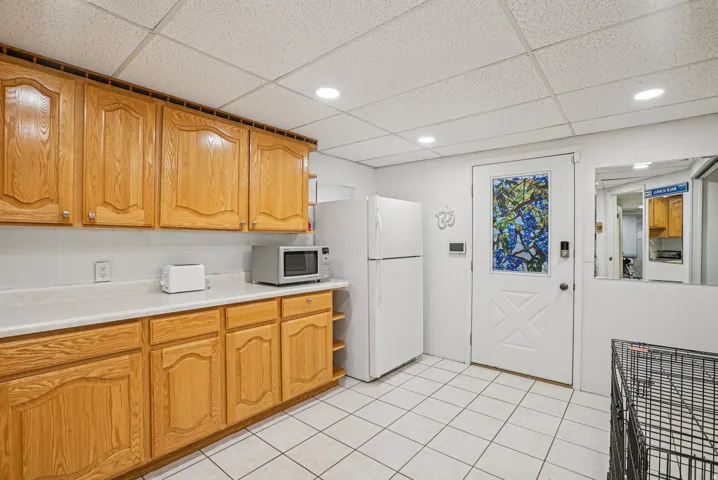 Kitchen featuring light countertops, a drop ceiling, white appliances, brown cabinets, and light tile patterned floors