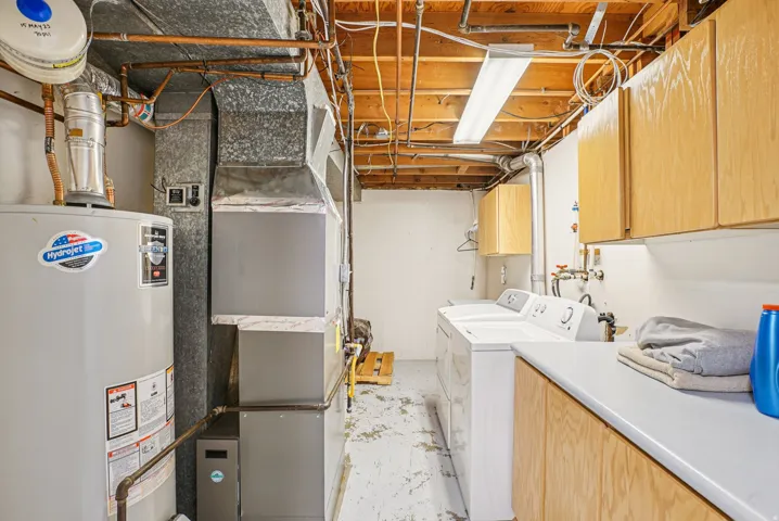 Laundry room featuring gas water heater, cabinet space, concrete flooring, heating unit, and washing machine and dryer