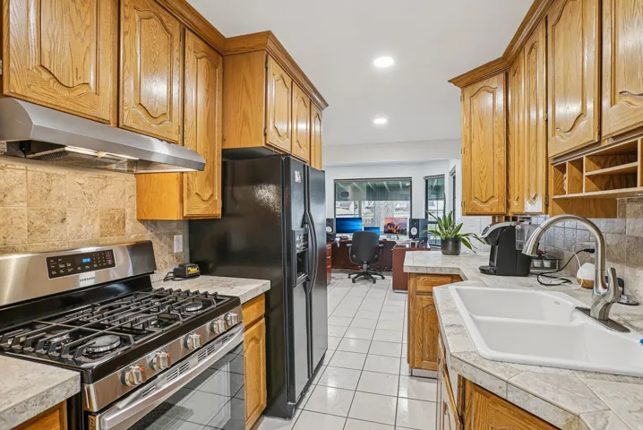 Kitchen featuring gas stove, brown cabinetry, decorative backsplash, under cabinet range hood, and recessed lighting