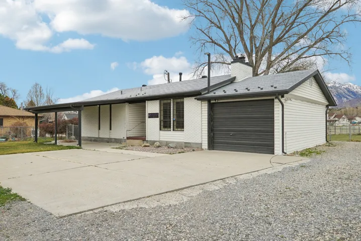 View of front of home with driveway, a garage, brick siding, and a chimney