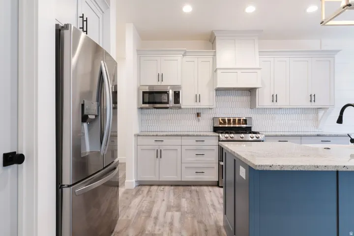 Kitchen featuring stainless steel appliances, granite countertops, white cabinetry, and recessed lighting