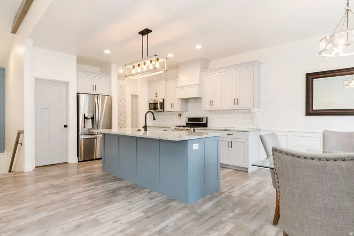 Kitchen featuring white cabinetry, appliances with stainless steel finishes, an island with sink, light wood finished floors, and light stone countertops