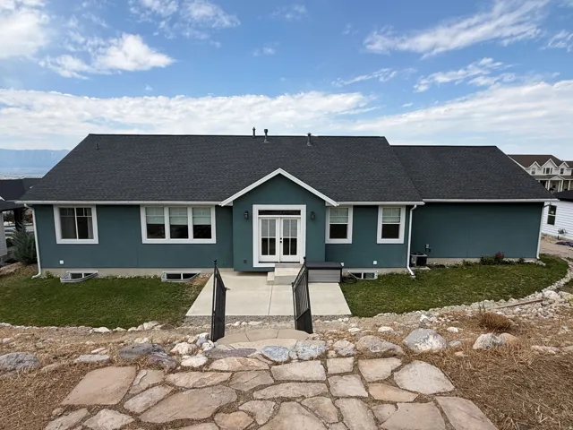Ranch-style residence featuring a dark asphalt shingle roof and teal stucco siding