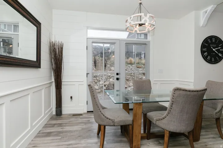 Dining room featuring french doors, a decorative wall, light wood finished floors, a chandelier, and a wainscoted wall