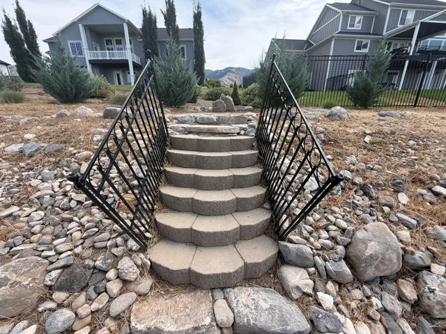 Tiered stone steps with wrought iron railings, set amidst a landscaped incline featuring natural rock accents and mature evergreen plantings