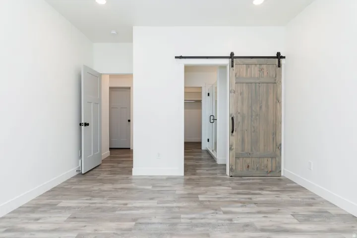 Unfurnished bedroom with a spacious closet, light wood finished floors, a barn door, and recessed lighting