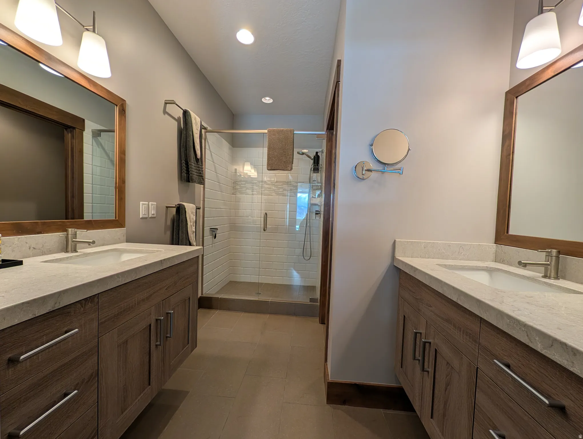 Full bathroom featuring two vanities, a shower stall, and recessed lighting