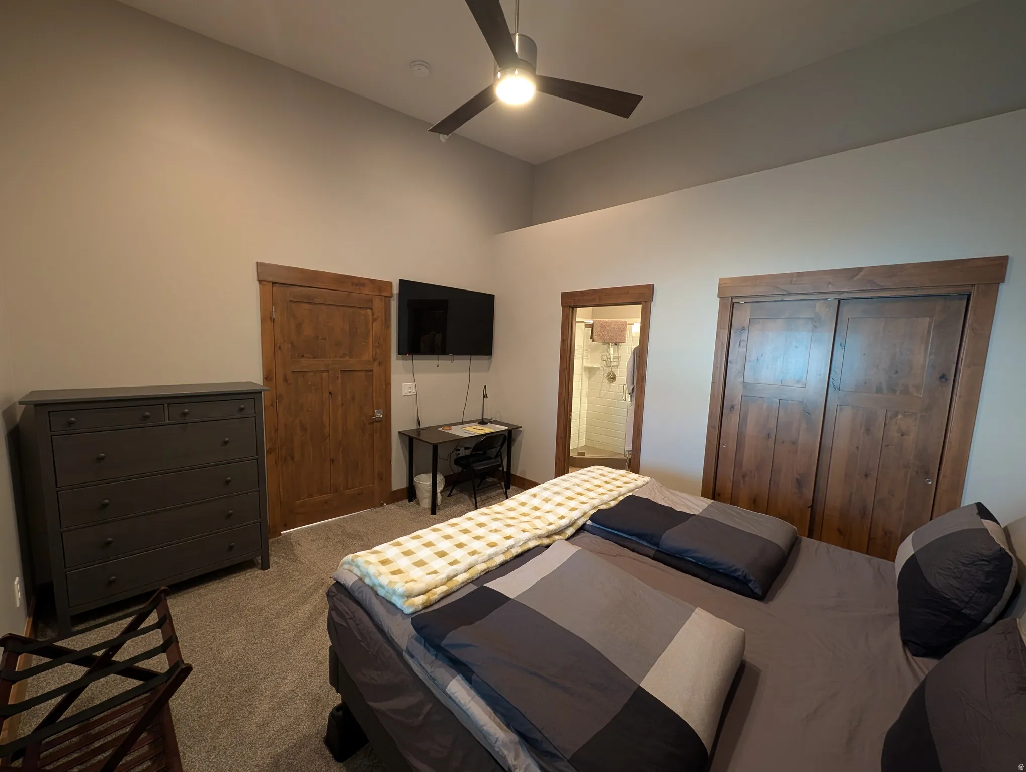 Carpeted bedroom featuring a ceiling fan, ensuite bath, and a towering ceiling