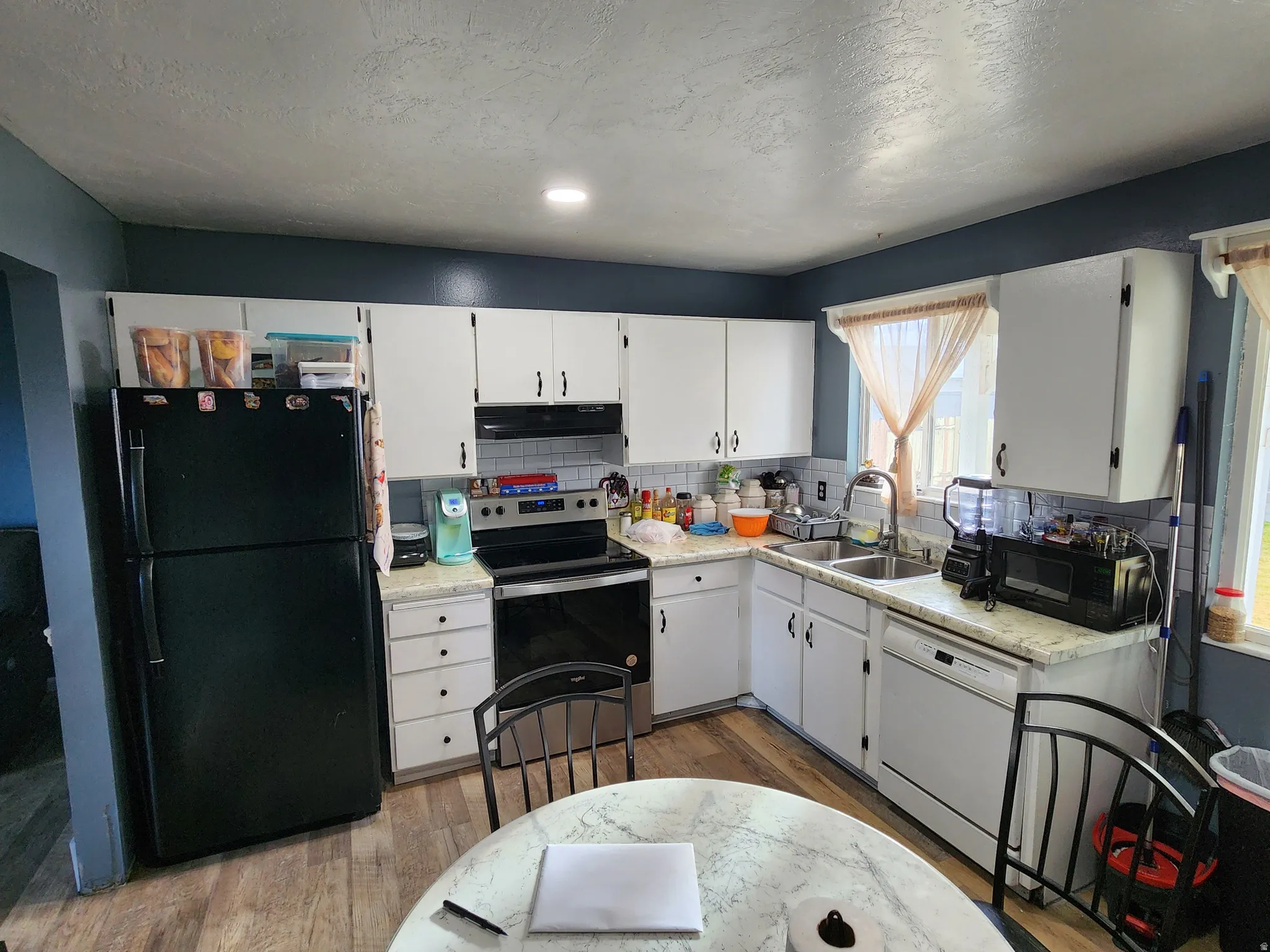 Kitchen featuring tasteful backsplash, black appliances, white cabinetry, light wood-type flooring, and a textured ceiling