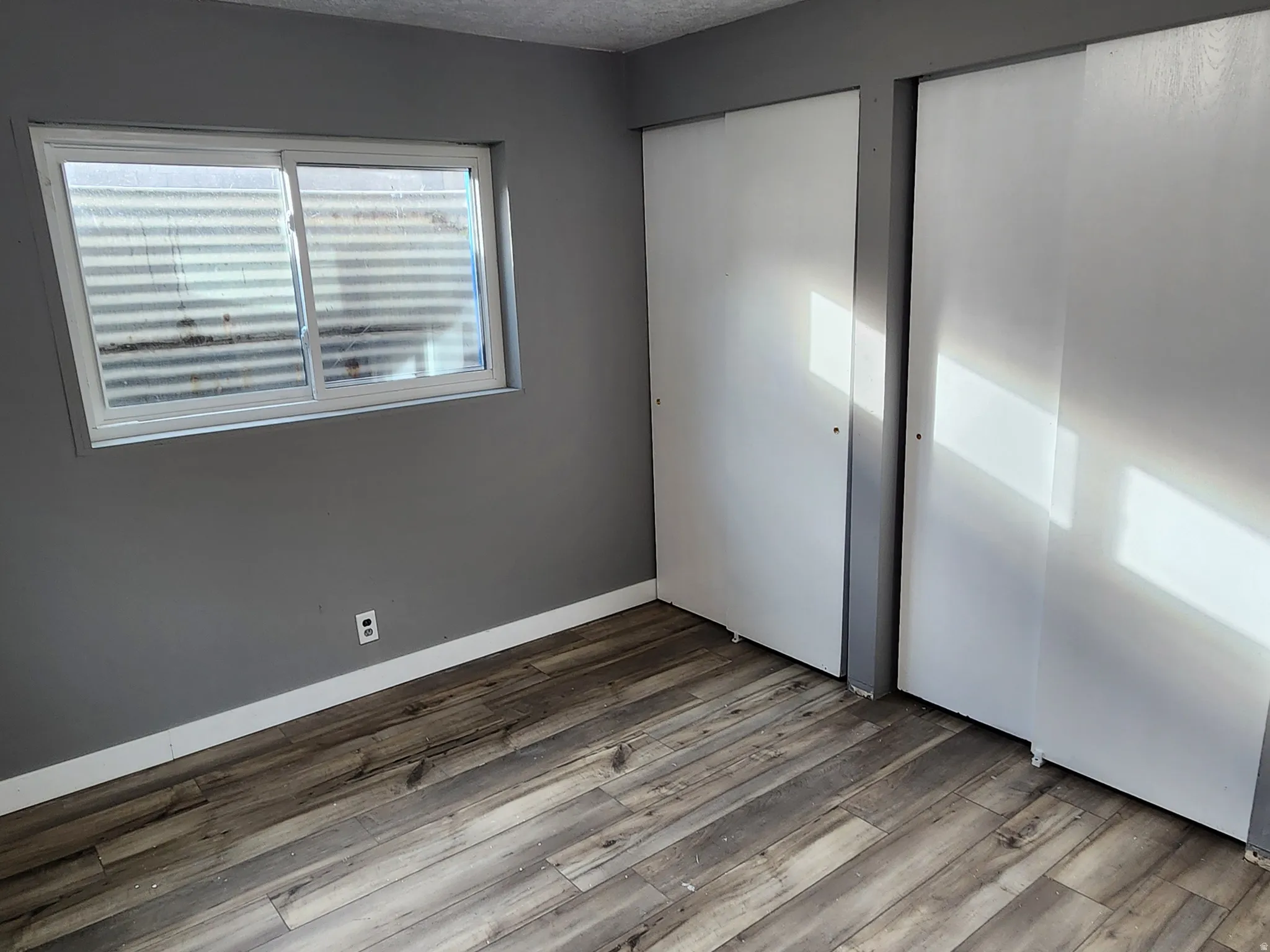 Unfurnished bedroom featuring a textured ceiling, wood finished floors, and two closets
