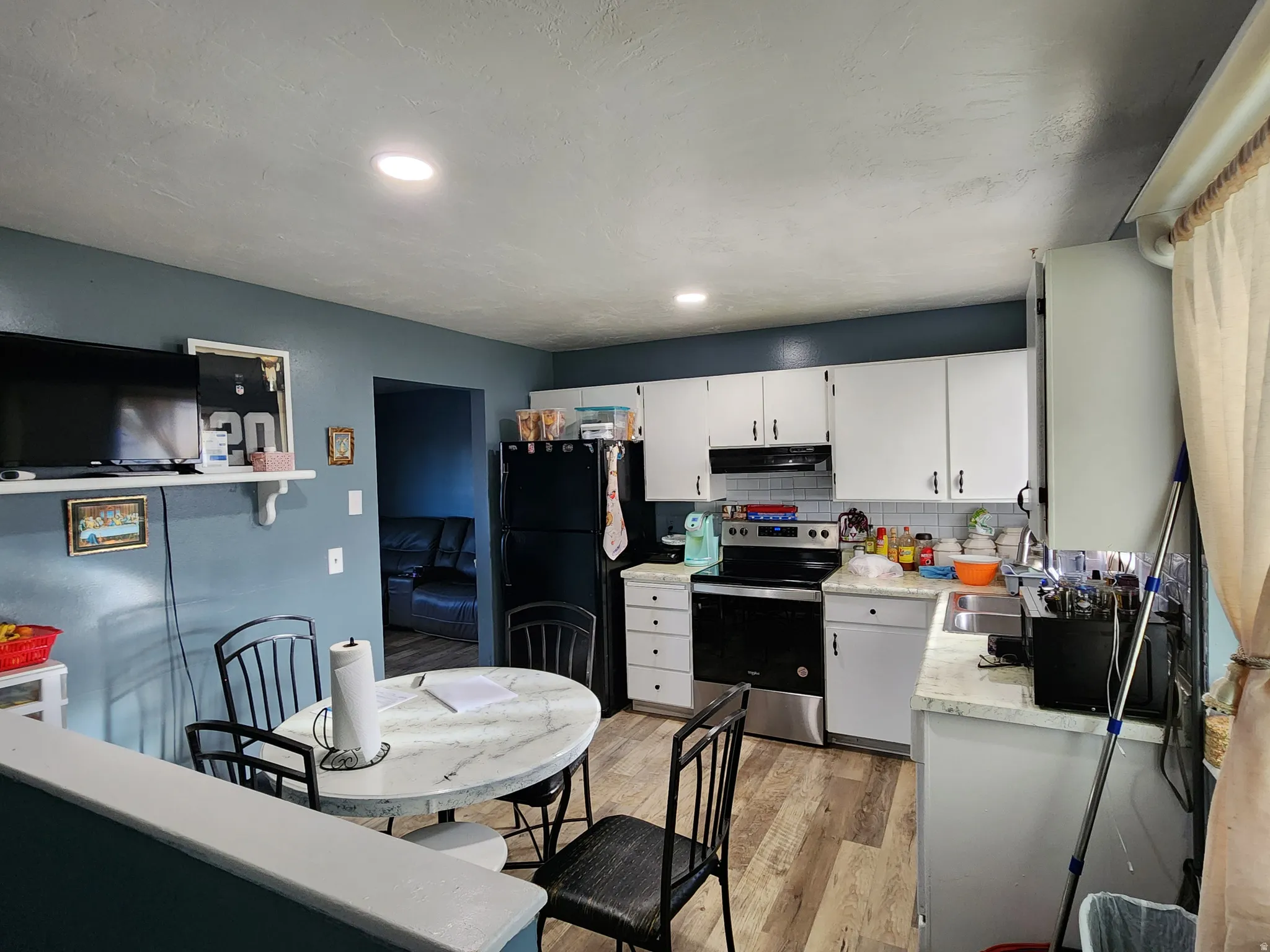 Kitchen with light countertops, electric stove, decorative backsplash, white cabinetry, and freestanding refrigerator