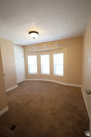 Unfurnished room featuring a textured ceiling, healthy amount of natural light, and dark colored carpet