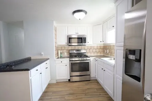 Kitchen with appliances with stainless steel finishes, white cabinets, light wood finished floors, backsplash, and a peninsula
