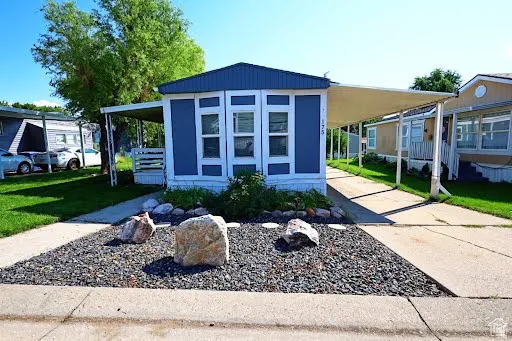 Manufactured / mobile home with driveway, a carport, covered porch, and a front lawn