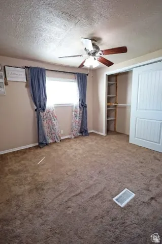 Unfurnished bedroom featuring a textured ceiling, a closet, ceiling fan, and light carpet