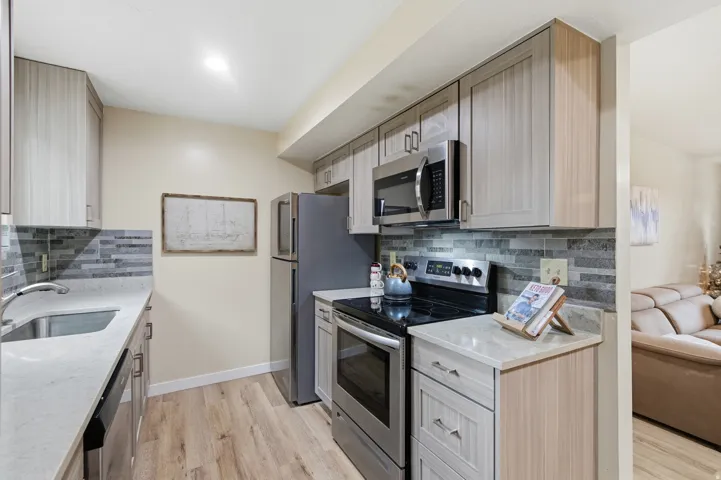 Kitchen featuring appliances with stainless steel finishes, light stone countertops, and tasteful backsplash