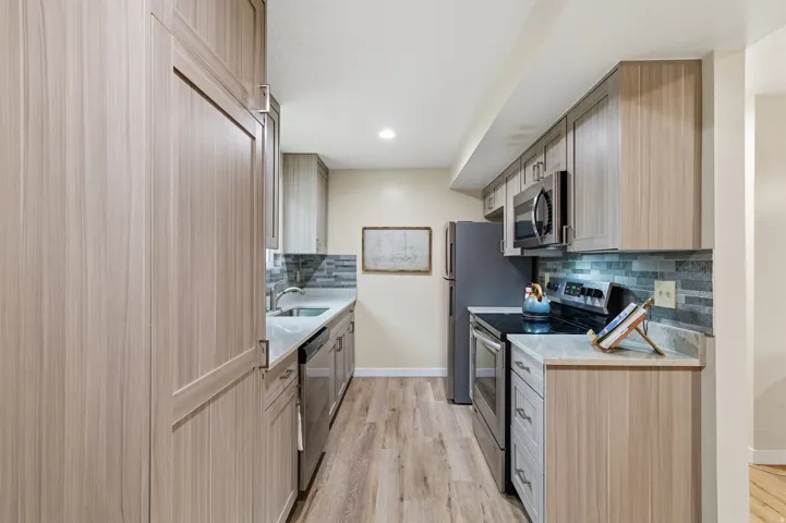 Kitchen featuring stainless steel appliances, light wood-style flooring, light brown cabinets, light stone counters, and recessed lighting