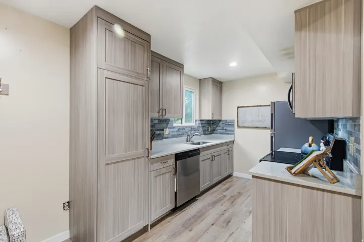 Kitchen with decorative backsplash, appliances with stainless steel finishes, light wood-style flooring, and light brown cabinetry