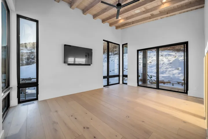 Unfurnished living room featuring a wood ceiling with exposed beams, healthy amount of natural light, a ceiling fan, and light wood-style floors
