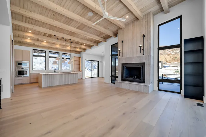 Unfurnished living room with a fireplace, light wood-style floors, ceiling fan, a wooden ceiling with exposed beams, and a towering ceiling