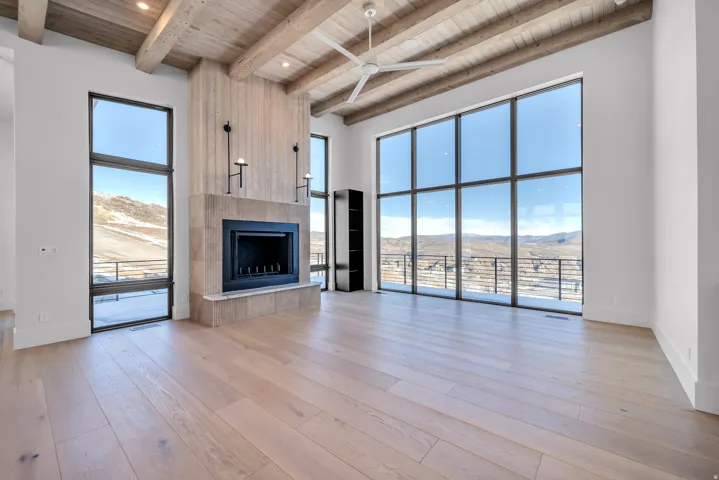 Unfurnished living room featuring a mountain view, a tile fireplace, light wood finished floors, a ceiling fan, and a wood ceiling with exposed beams