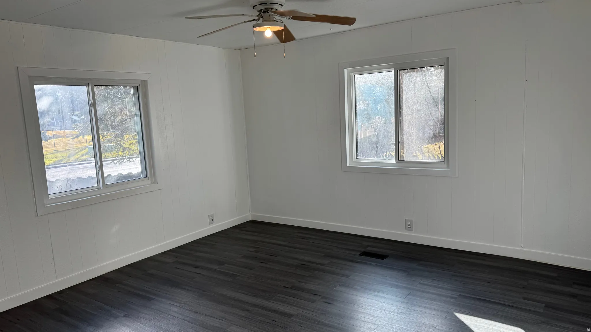 Empty room with dark wood-style flooring, wood walls, and a ceiling fan
